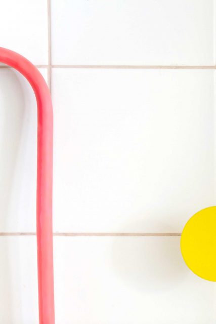 Détail sur la mise en valeur colorée et graphique du système de plomberie des points d'eau pour enfants en écho au mur orange fluo de la cage d'escalier attenante pour le projet de l'Ecole Montessori Square Paris 18.