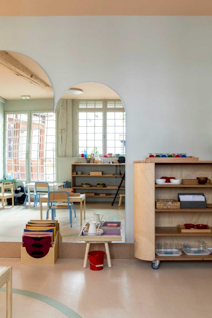 Vue de l'espace manipulation et motricité du projet de l'Ecole Montessori Square Paris 18 avec un grand miroir sur mesure à tête cintré pour réfléchir la lumière de la cour attenante et ouvrir l'espace étroit ainsi que son meuble mobile de rangement permettant d'organiser l'espace et créer dans cet espace ouvert divers zone d'apprentissage..