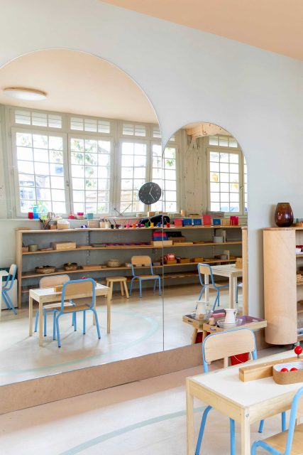 Vue de l'espace manipulation et motricité du projet de l'Ecole Montessori Square Paris 18 avec ses teintes vert-de-gris et rose pâle pour un écrin doux aux divers plateaux colorés de manipulation / apprentissage en autonomie ainsi que son très beau miroir sur mesure à tête cintré.