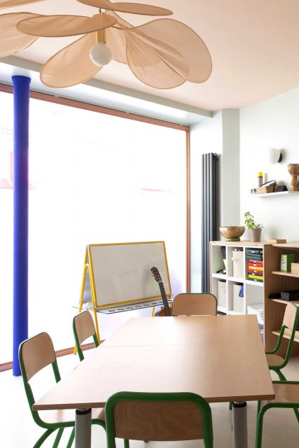 Vue sur l'espace de travail donnant sur la rue de l'Ecole Montessori Square Paris 18, baigné de lumière et fort de son parti pris coloré rose et vert-de-gis, une jolie suspension en tissu Pale Georges détourne les codes de l'école et initie à l'art de la légèreté.